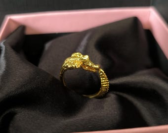 May include: A gold ring with a detailed alligator head design. The ring is in a pink box with black velvet lining.