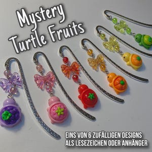 Könnte beinhalten: Eine Auswahl an Metall-Lesezeichen mit bunten Schildkröten- und Schleifenanhängern in Lila, Rosa, Rot, Orange und Grün. Der Text "Mystery Turtle Fruits" ist zu sehen. Leseaccessoire.