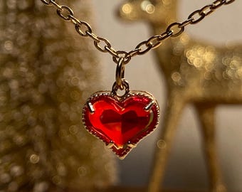 Könnte beinhalten: Eine goldfarbene Halskette mit einem herzförmigen Anhänger. Der Anhänger ist leuchtend rot mit einem goldfarbenen Rand. Die Kette ist filigran und hat ein klassisches Kettendesign. Es handelt sich wahrscheinlich um ein Schmuckstück.