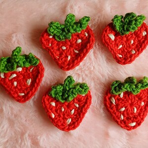 Peut inclure: Cinq appliques en crochet en forme de fraises avec des feuilles vertes. Les fraises sont rouges avec des points blancs et les feuilles sont vertes.