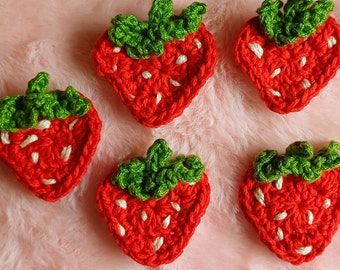 May include: Five crocheted strawberry appliques with green leaves. The strawberries are red with white stitching and the leaves are green.