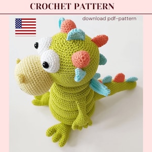 May include: A crocheted green dinosaur toy with blue and pink accents. The dinosaur has large white eyes and a long tail.