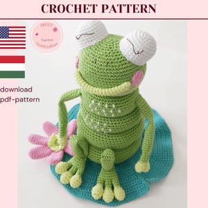 Op de afbeelding: Een gehaakte kikker met grote witte ogen, een lichtgroen lichaam en een gele kraag zit op een blauwe waterlelie. Een roze en witte bloem staat naast de kikker. De tekst "CROCHET PATTERN" staat bovenaan.