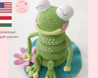 May include: A crocheted frog with large white eyes, a light green body, and a yellow collar sits on a blue lily pad. A pink and white flower is next to the frog. The text "CROCHET PATTERN" is at the top.