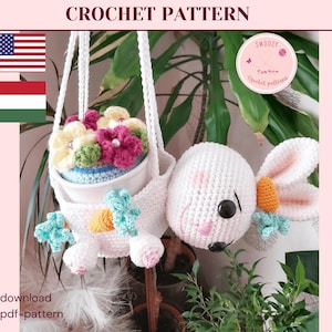 Könnte beinhalten: Ein weißer gehäkelter Hase hält einen gehäkelten Blumentopf mit einem weißen Topf und bunten Blumen. Der Hase hängt an einer weißen Schnur. Das Bild enthält den Text "Crochet Pattern" und "Download pdf-pattern".