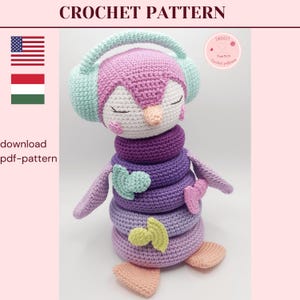 Puede incluir: Un juguete apilable con forma de pingüino tejido a ganchillo en tonos morado, rosa y verde. El pingüino lleva auriculares y tiene una pila de anillos para el cuerpo. El texto "CROCHET PATTERN" está en la parte superior. El texto "download pdf-pattern" está a la izquierda.