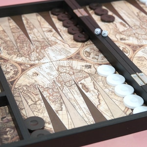 May include: A backgammon set featuring a vintage map design. The board is dark brown, with white and brown game pieces, and two dice. The game board is open and ready to play.