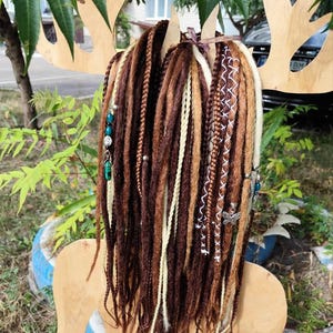 K&ouml;nnte beinhalten: Braune, blonde und wei&szlig;e synthetische Dreadlocks mit t&uuml;rkisfarbenen und silbernen Perlen. Die Dreadlocks sind mit einem braunen Band zusammengebunden.