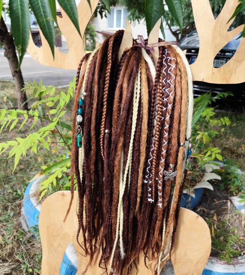 K&ouml;nnte beinhalten: Braune, blonde und wei&szlig;e synthetische Dreadlocks mit t&uuml;rkisfarbenen und silbernen Perlen. Die Dreadlocks sind mit einem braunen Band zusammengebunden.