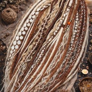 Op de afbeelding: Een verzameling bruine, witte en blonde dreadlocks, sommige versierd met decoratieve stiksels en kralen. De dreadlocks zijn in een waaier gerangschikt en tonen verschillende texturen en stijlen. De algehele esthetiek is boheems en natuurlijk.