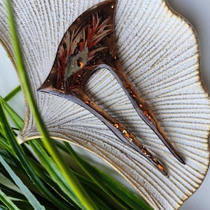 May include: A brown and gold hair comb with a floral design. The comb is made of resin and has a unique, abstract shape.