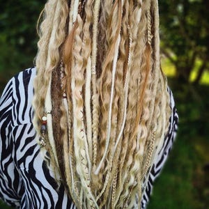 May include: Blonde dreadlocks with white and brown synthetic hair extensions. The dreadlocks are styled in a wavy pattern and have beads and charms.