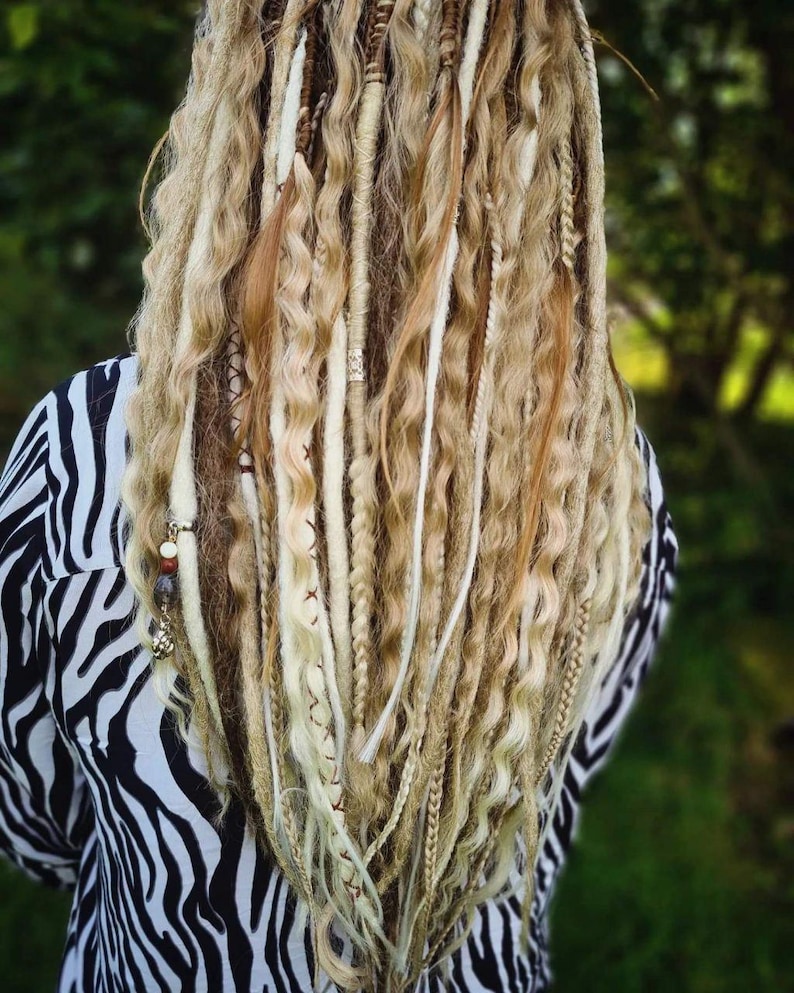May include: Blonde dreadlocks with white and brown synthetic hair extensions. The dreadlocks are styled in a wavy pattern and have beads and charms.