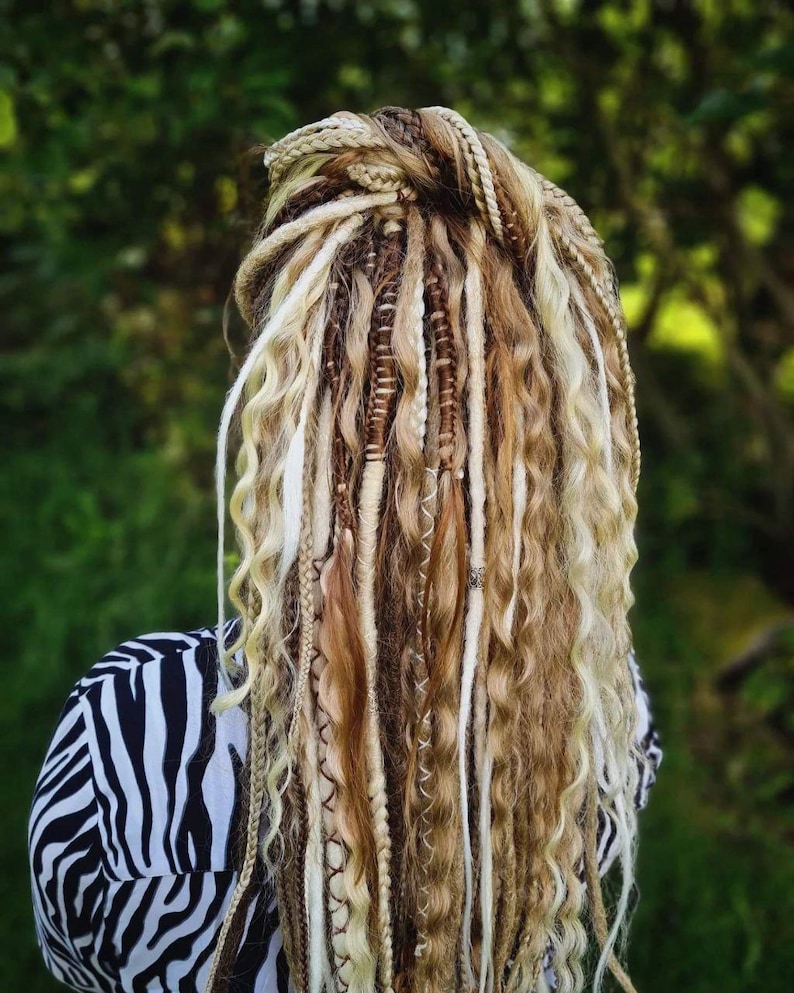 May include: A person with long, blonde dreadlocks with brown and white accents. The dreadlocks are pulled back into a ponytail.