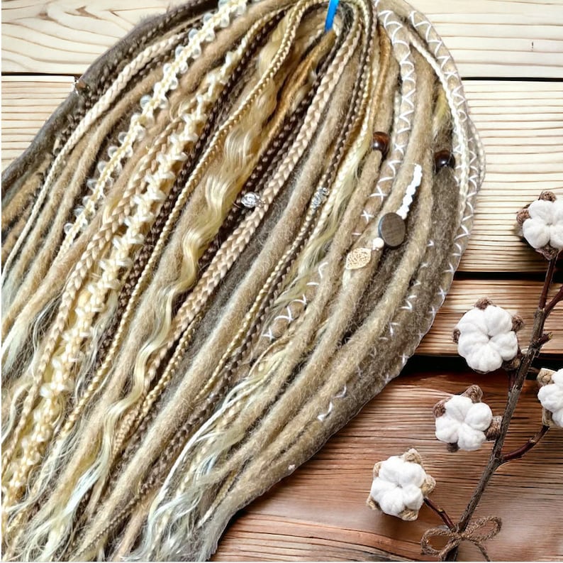 May include: A set of brown, blonde, and white synthetic dreadlocks with beads and charms. The dreadlocks are arranged in a fan shape and are lying on a wooden surface.