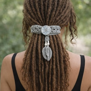 Puede incluir: Un accesorio para el cabello de ganchillo gris con un botón decorativo y un adorno colgante en forma de hoja con perlas de imitación. El accesorio para el cabello está diseñado para usarse en la parte posterior de la cabeza, agregando un toque de encanto hecho a mano.