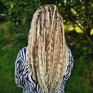 May include: A person with long, blonde dreadlocks with brown and white accents. The dreadlocks are styled in a wavy pattern and fall to the person's waist.