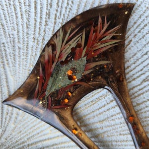 May include: A brown resin hair comb with a unique design featuring dried flowers and gold glitter embedded in the resin.