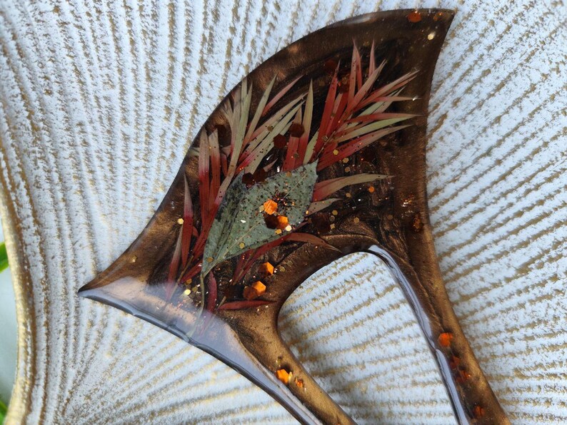May include: A brown resin hair comb with a unique design featuring dried flowers and gold glitter embedded in the resin.