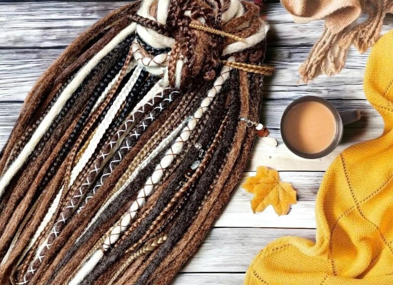 K&ouml;nnte beinhalten: Nahaufnahme eines B&uuml;ndels brauner, wei&szlig;er und schwarzer synthetischer Dreadlocks. Die Dreadlocks sind oben zusammengebunden und haben verschiedene Verzierungen, darunter Perlen und N&auml;hte.
