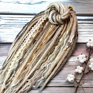May include: A set of brown, blonde, and white synthetic dreadlocks with a variety of textures, including wavy, straight, and braided. The dreadlocks are tied together with a brown string and have beads and charms.