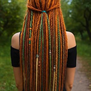 May include: A person's back is shown, with long, orange and brown dreadlocks. The dreadlocks are adorned with green and blonde strands, and decorative beads. The hair is styled with a teal hair tie, and the person is wearing a black off-the-shoulder top.