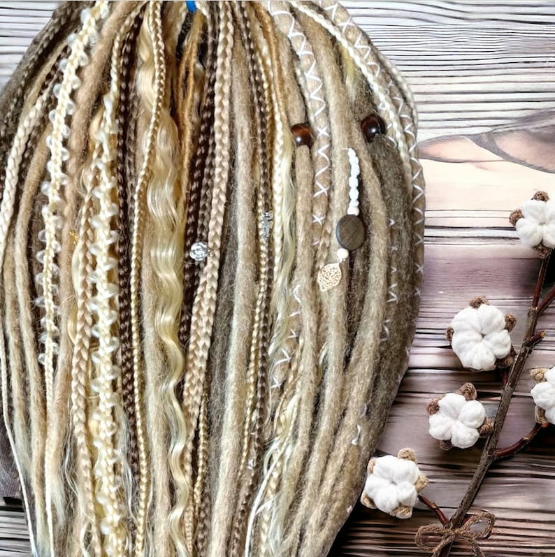 May include: A set of brown, blonde, and white synthetic dreadlocks with beads and charms. The dreadlocks are arranged in a fan shape and are displayed against a wooden background.