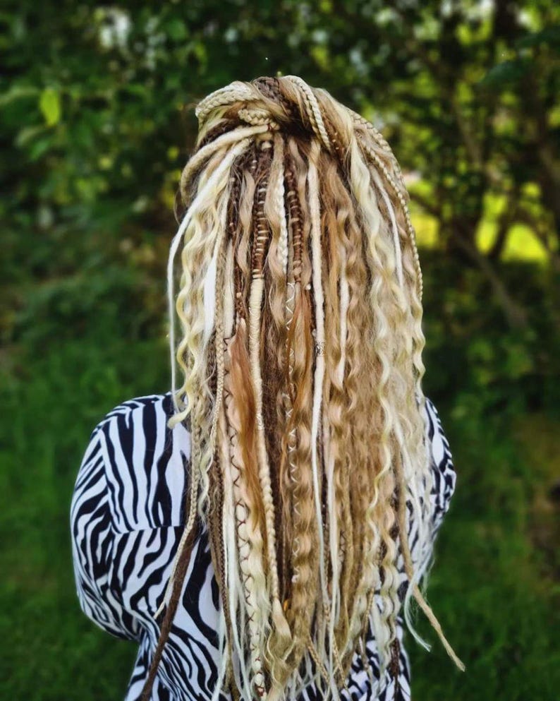 May include: A person with long, blonde, and brown dreadlocks with beads woven in. The dreadlocks are pulled back into a ponytail. The person is wearing a black and white zebra print shirt.
