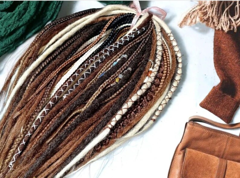 K&ouml;nnte beinhalten: Ein B&uuml;ndel brauner, schwarzer und wei&szlig;er synthetischer Dreadlocks mit wei&szlig;en N&auml;hten. Die Dreadlocks sind mit einem rosa Band zusammengebunden.