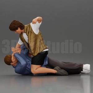 May include: A person wearing a brown vest and black shorts is holding another person down by the arm. The person on the bottom is wearing a blue shirt and grey trousers.