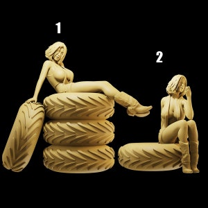Puede incluir: Dos figuras de mujeres en una pose de pin-up. Una mujer está sentada en una pila de cuatro neumáticos, la otra está sentada en un solo neumático. Ambas figuras llevan pantalones cortos y botas.