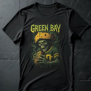 Könnte beinhalten: Schwarzes T-Shirt mit einer skelettartigen Figur in Football-Uniform, die einen Football hält. Das Design enthält die Worte "GREEN BAY" in einer verwitterten, gelben Schriftart, und die Figur trägt einen Cheesehead. Das Shirt hat einen Rundhalsausschnitt.