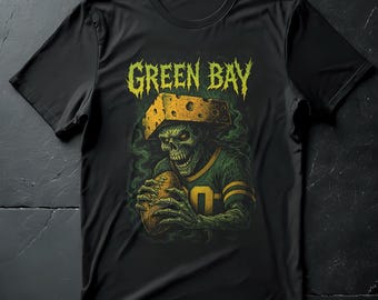 May include: Black t-shirt featuring a skeletal figure in a football uniform, holding a football. The design includes the words "GREEN BAY" in a distressed, yellow font, and the figure wears a cheesehead. The shirt has a crew neck.