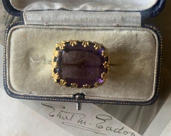 May include: A purple gemstone ring set in a gold setting. The ring is in a velvet-lined box with the inscription "Robert Crawford, Watchmaker & Jeweller, Cumnock".