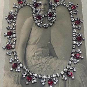 Peut inclure: Un ensemble vintage de collier et de bracelet. Les bijoux présentent des strass clairs et étincelants et des pierres rouges ovales vibrantes. Le collier et le bracelet sont présentés sur une photographie vintage.