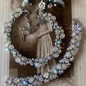 Könnte beinhalten: Ein Set aus zwei vintage-artigen, regenbogenfarbenen Strass- und Kunstperlen-Halsketten. Die Halsketten sind silberfarben und haben ein florales Design. Die Halsketten werden auf einem Vintage-Foto gezeigt.