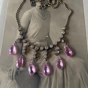 May include: A vintage necklace featuring a silver chain and a delicate design of clear rhinestones and pink glass teardrop pendants.
