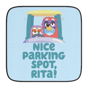Op de afbeelding: Een blauwe autozonnescherm met twee cartoonfiguren die rijden. De tekst op de zonneklep luidt "Nice Parking Spot, Rita!"