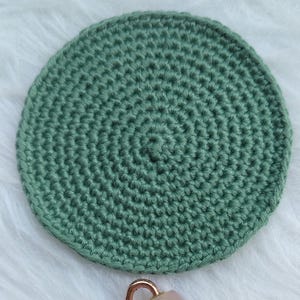 Peut inclure: Un disque de coton crocheté vert sauge circulaire avec un motif de points serrés et uniformes, accompagné d'un rouleau facial doté d'une tête en pierre de quartz rose lisse et polie et d'une monture en métal or rose avec un manche assorti.