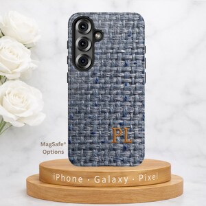 May include: A smartphone case with a woven blue and gray pattern, featuring the initials "PL" in gold. The case is displayed on a wooden stand with the text "iPhone · Galaxy · Pixel" and "MagSafe Options".