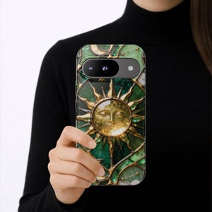 K&ouml;nnte beinhalten: Eine gr&uuml;n-goldene Handyh&uuml;lle mit einem Sonnendesign. Die H&uuml;lle hat eine goldene Sonne mit einem Gesicht in der Mitte, umgeben von goldenen Akzenten und einem gr&uuml;nen Hintergrund. Die H&uuml;lle wird von einer Person gehalten.
