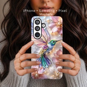 May include: A phone case featuring a colorful hummingbird design with floral accents and the name "Mallory". The case is decorated with pearls and has the text "iPhone • Samsung • Pixel MagSafe".