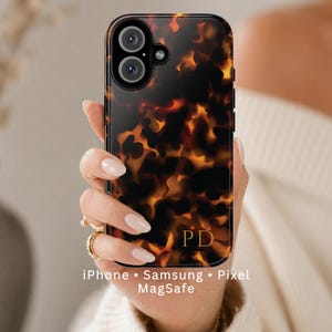 May include: A tortoiseshell-patterned phone case with the initials "PD" in gold. The case is designed for iPhone, Samsung, and Pixel phones and is MagSafe compatible. The case has a glossy finish and a black border.