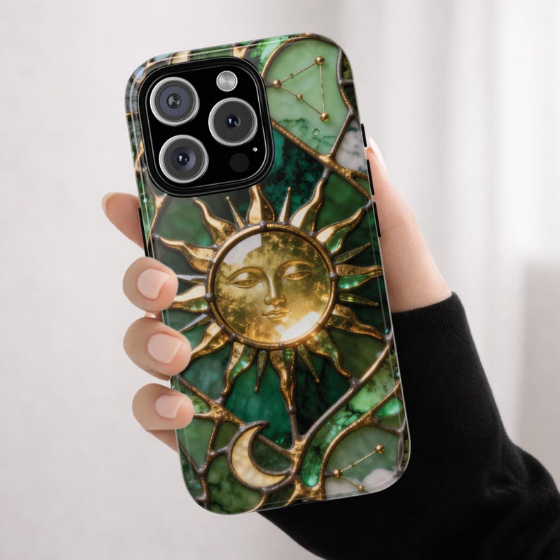Green emerald stained glass phone case featuring a gold sun with sculpted rays centered on the design, surrounded by crescent moon and star details. The case displays rich green marble textures with metallic gold lead lines, creating a luminous celestial pattern. Shown as a MagSafe-compatible protective phone case for iPhone, Samsung, and Google Pixel, photographed against a clean white background with a polished finish.