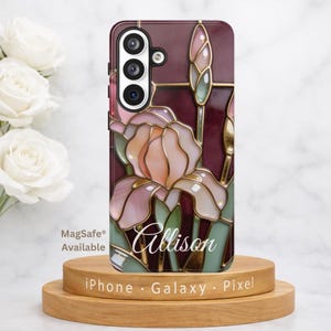 May include: A phone case with a stained-glass design featuring a pink and peach iris flower. The case has a burgundy background with gold accents and the name "Allison" in script. The case is displayed on a wooden stand.