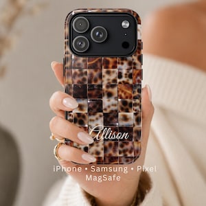 May include: A phone case with a tortoiseshell pattern in shades of brown and cream, held in a person's hand. The case has a glossy finish and a grid-like design. The name "Allison" is written in cursive. The text "iPhone • Samsung • Pixel MagSafe" is at the bottom.