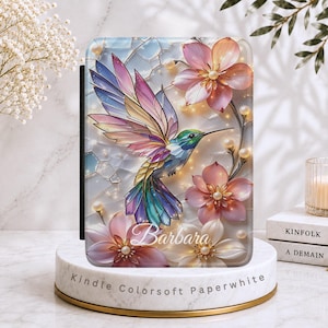 May include: A Kindle Colorsoft Paperwhite e-reader case featuring a vibrant stained-glass style illustration of a hummingbird in flight surrounded by pink flowers and small white pearls. The name Barbara is printed in white script at the bottom.
