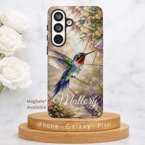 May include: A phone case featuring a stained-glass style hummingbird design. The hummingbird has colorful wings and is set against a floral background. The name "Mallory" is written in cursive. The case is available with MagSafe.
