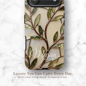 May include: A phone case featuring a stained glass-inspired pattern of copper-toned branches and green leaves against a cream-colored background. The name Megan is written in white cursive script across the center of the design.