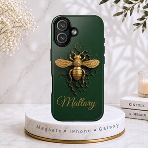 May include: A dark green phone case featuring a gold-colored bee graphic centered over a black honeycomb pattern. The name Mallory is printed in gold script below the bee. The case has a camera cutout at the top left and a smooth finish.
